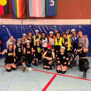VRDL and guest skaters after a sweat session smiling for the camera in front of Aboriginal, Rainbow, and Trans Flags.